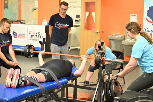 Dairyland Sports staff and volunteers spot a participant performing a bench press as part of the Fitness Foundations program